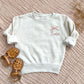 natural heather toddler crewneck with embroidered name and bow on the left chest in mauve thread.