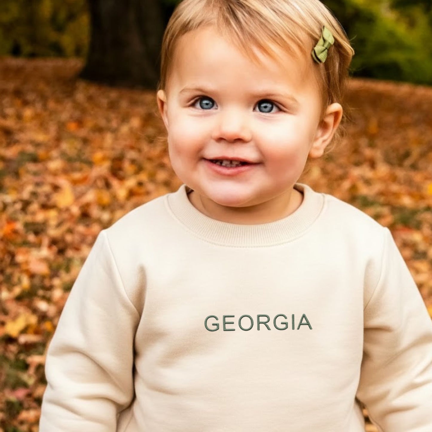 little girl wearing a natural crewneck sweatshirt with georgia embroidered in eucalyptus thread on the center chest