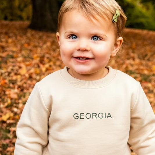 little girl wearing a natural crewneck sweatshirt with georgia embroidered in eucalyptus thread on the center chest