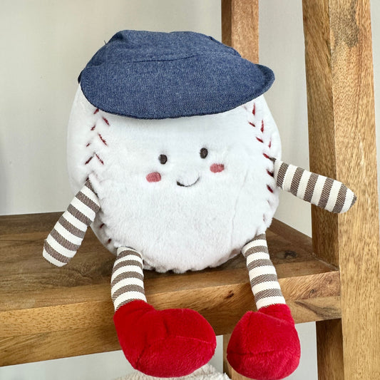 Stuffed toy resembling a baseball with a face, blue cap, and red shoes on a wooden surface.