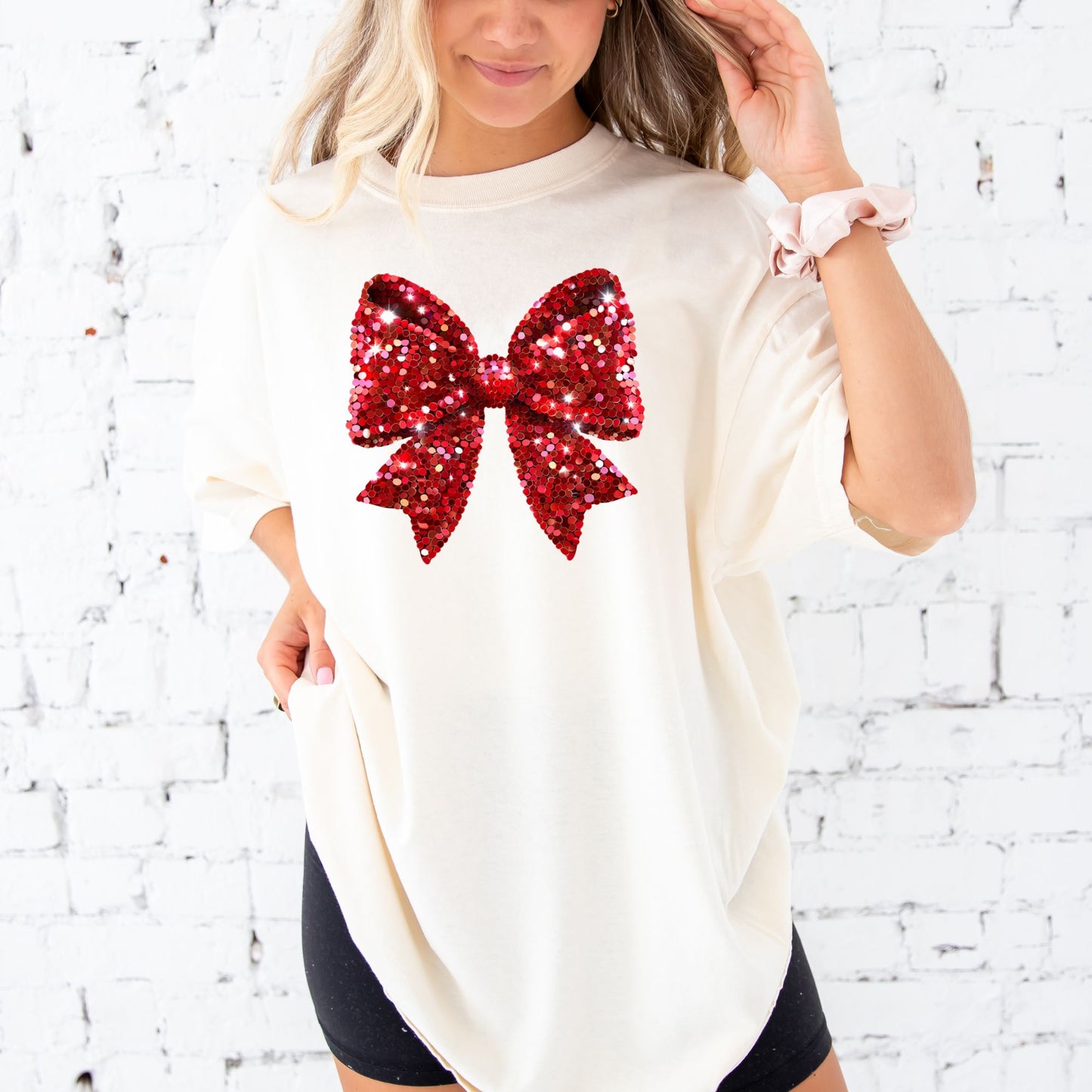 young woman wearing an ivory comfort colors t-shirt with large printed glitter red bow across the front of the tee