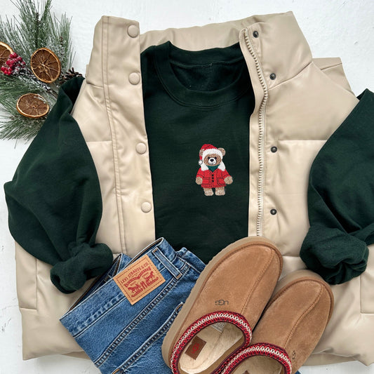 Beige jacket, green shirt with teddy bear design, blue jeans, and brown slippers on a white background.