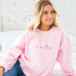 girl wearing a light pink crewneck with custom embroidered design of FAITH with a cross for the T in pink thread.