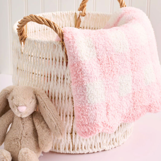 Wicker basket with pink and white blanket and brown plush bunny toy on a light background