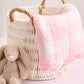 Wicker basket with pink and white blanket and brown plush bunny toy on a light background