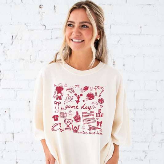 Woman wearing an ivory t-shirt with red football doodled icons and game day text 
