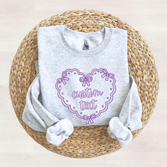 Ash grey sweatshirt with a printed purple doily heart design featuring a place for 'custom text' in the center of the heart