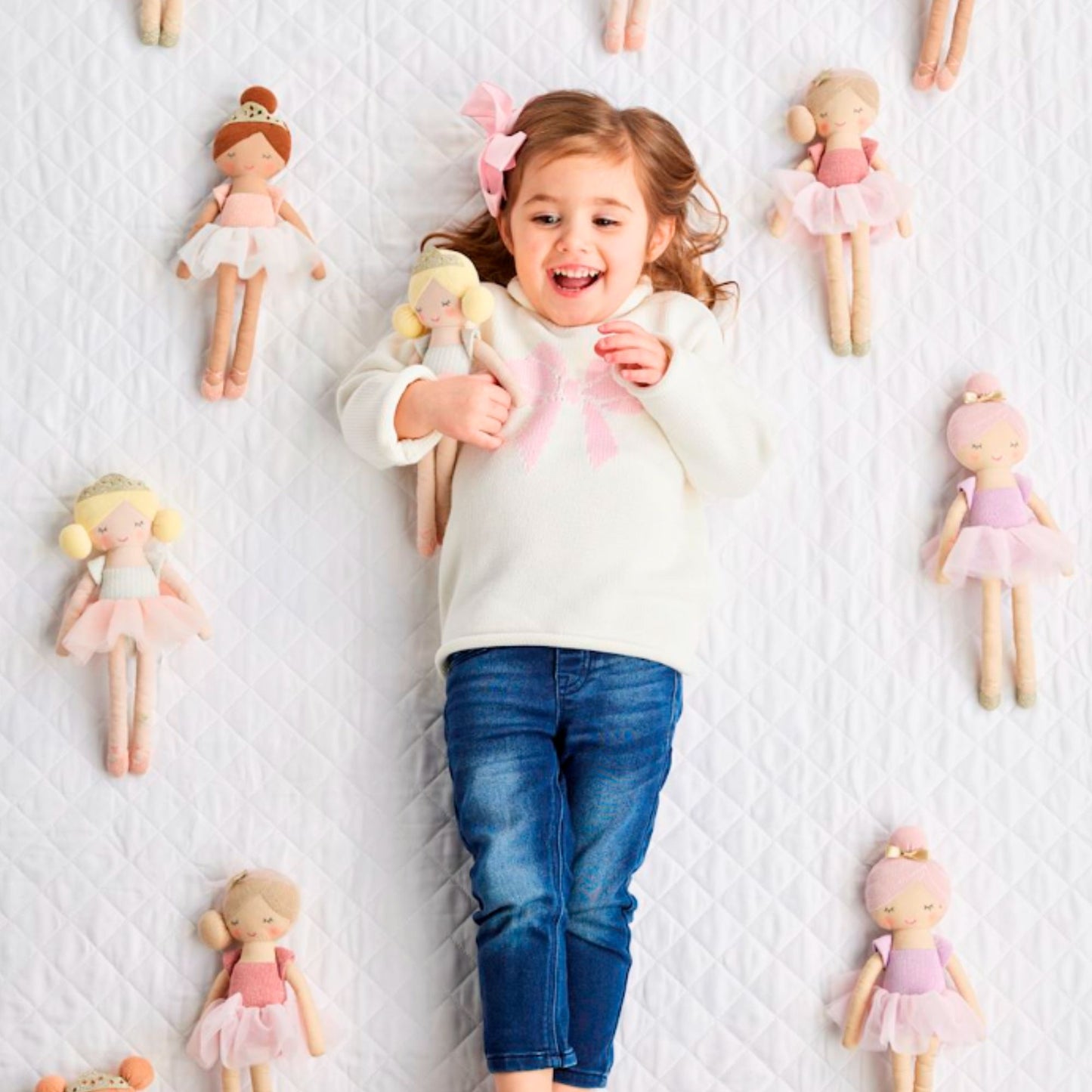 Child surrounded by dolls on a textured white surface