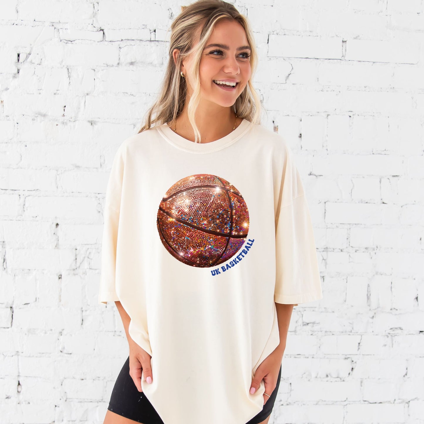 young woman wearing an ivory comfort colors t-shirt with large glitter basketball print with uk basketball text wrapping around the ball in royal ink