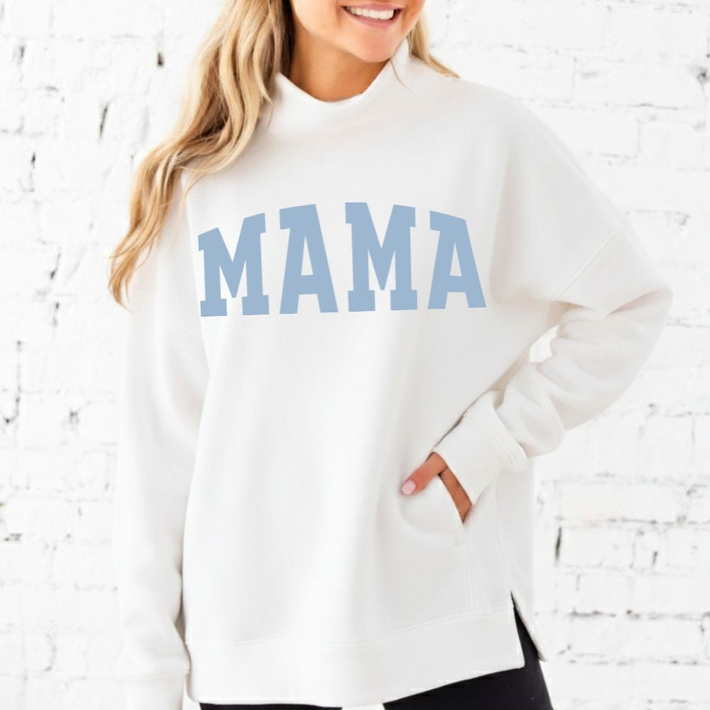 Woman wearing a white sweatshirt with 'MAMA' printed in blue on a white brick background