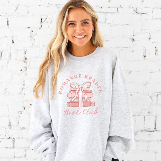 woman wearing an ash crewneck sweatshirt with a romance reader book club pink bow printed design