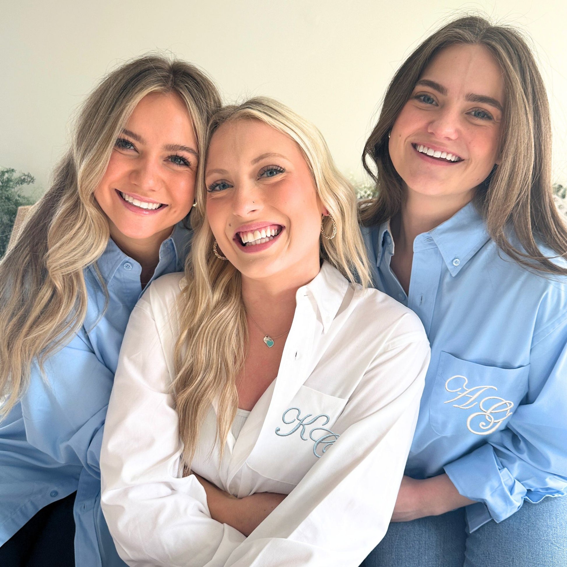 Three women wearing embroidered shirts posing together.
