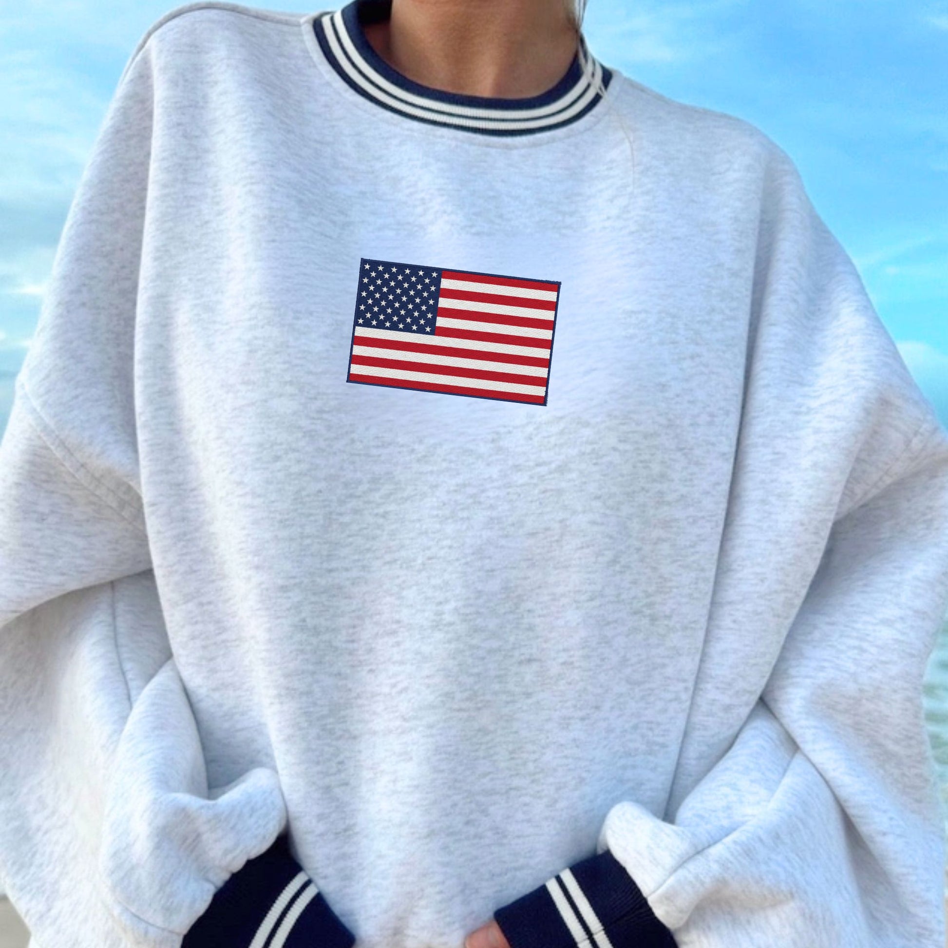 Gray sweatshirt with American flag embroidery against a blue sky background