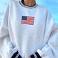 Gray sweatshirt with American flag embroidery against a blue sky background