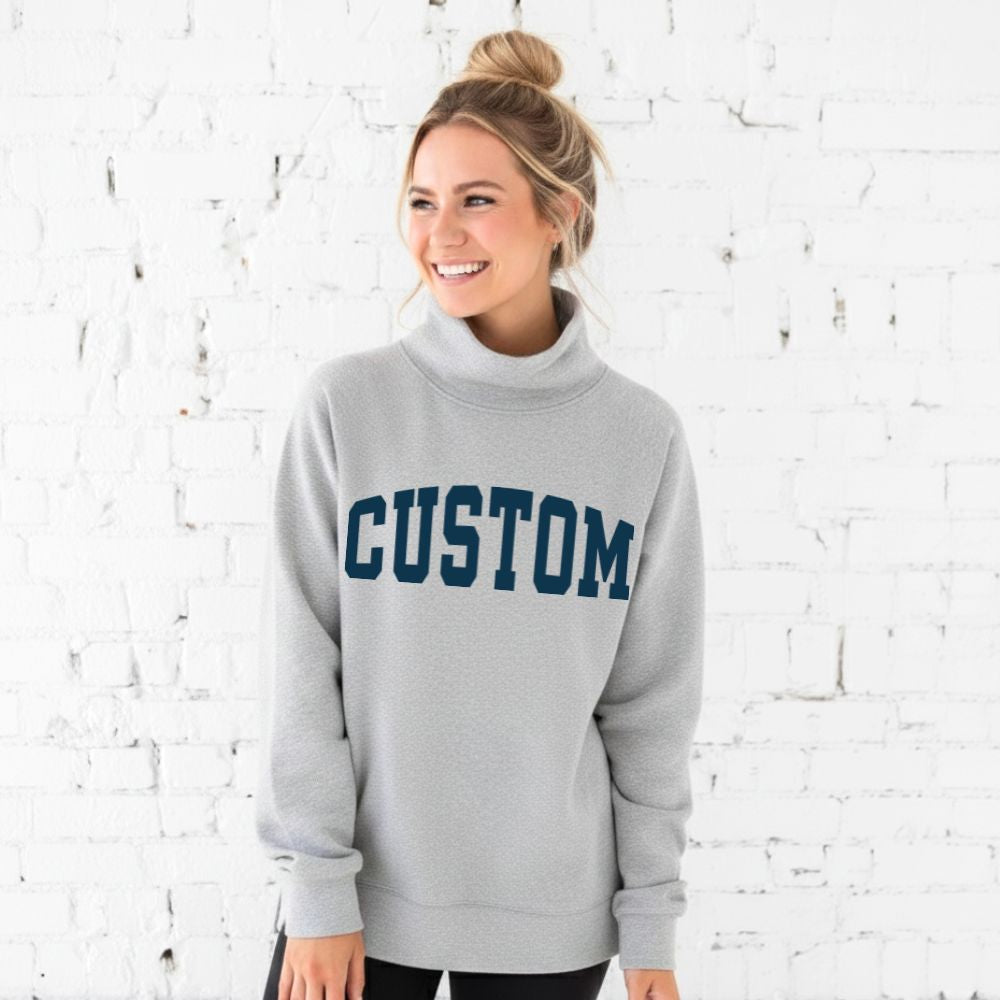 Woman wearing a gray sweatshirt with 'CUSTOM' printed on it against a white brick wall.