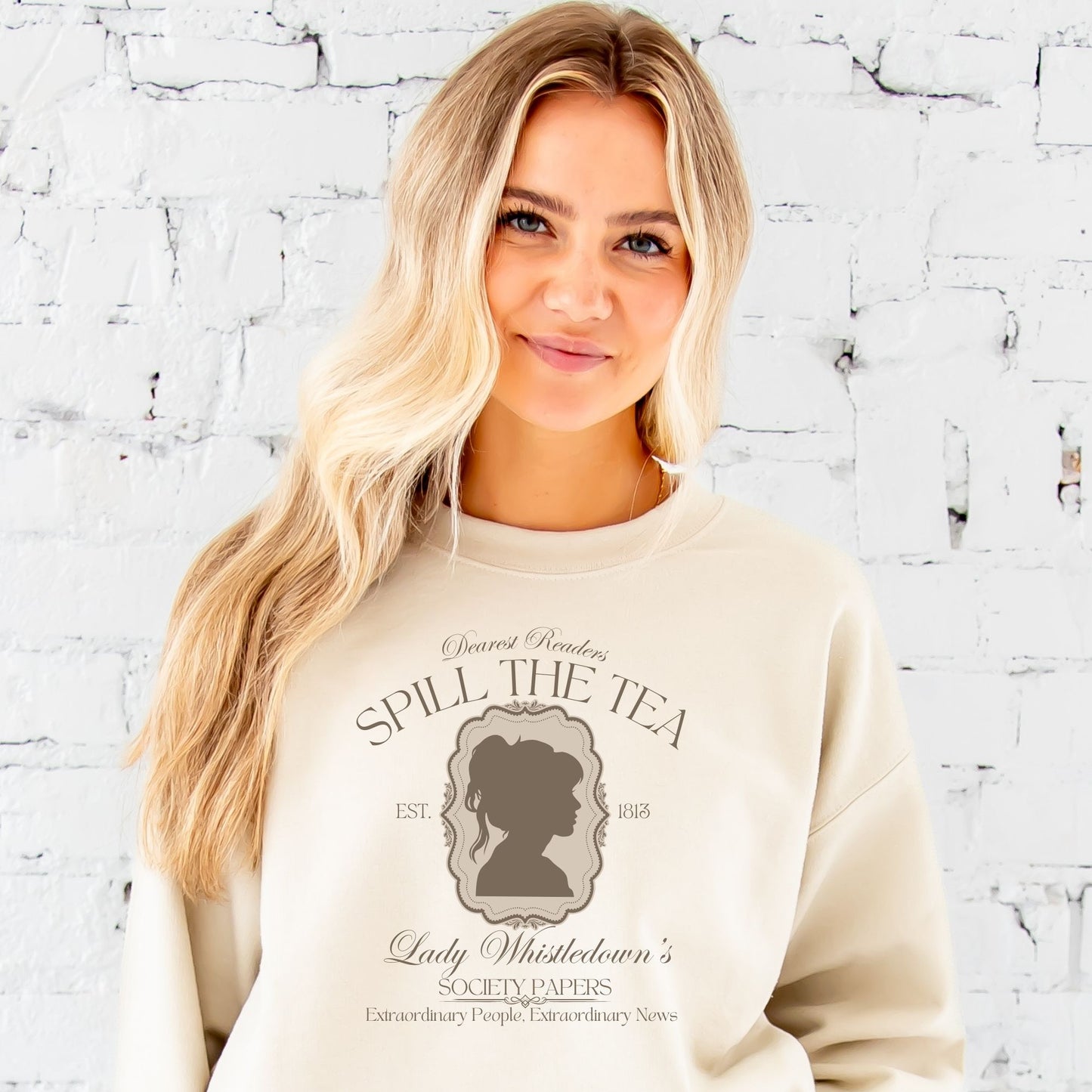 WOMAN WEARING A SAND SWEATSHIRT WITH A SPILL THE TEA LADY WHISTLEDOWN PRINTED DESIGN