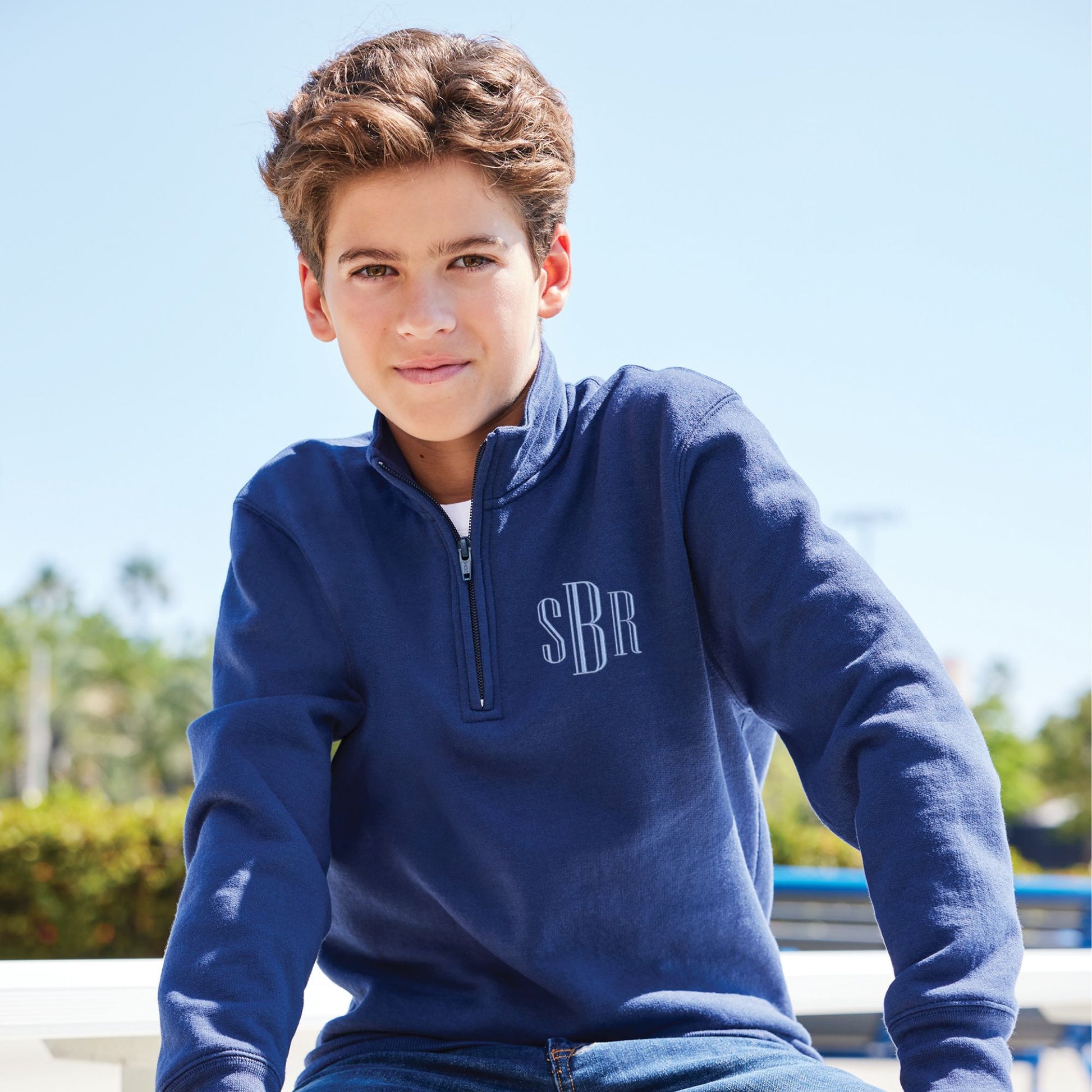 boy wearing a navy quarter zip sweatshirt with a custom embroidered monogram in a powder blue thread