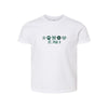 A white short-sleeve crewneck t-shirt featuring a St. Pius X themed graphic on the chest with green flowers, a paw print, and a heart, displayed on a clean white background