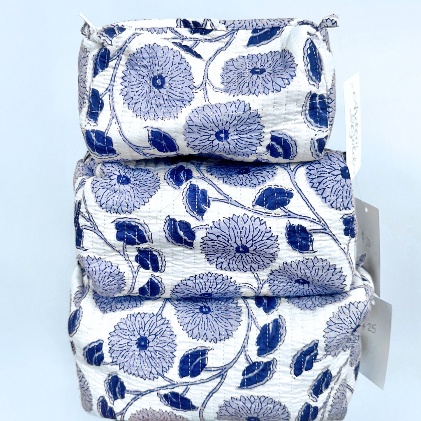 Stack of quilted pouches with blue floral pattern on a light blue background