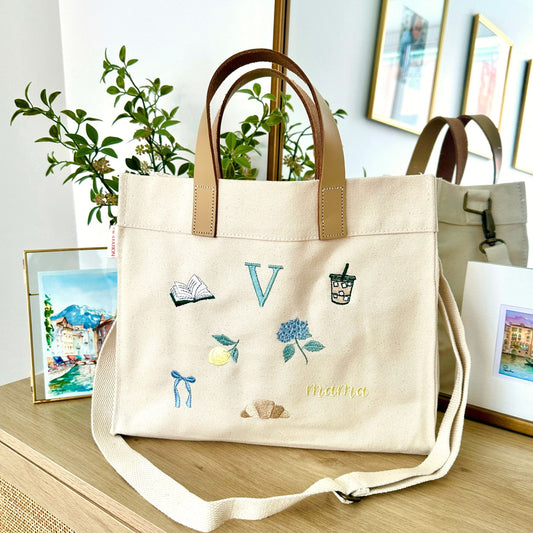 Beige tote bag with embroidered designs on a wooden surface