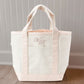 canvas tote bag with pink trim and edwardian script font monogram on a wooden floor.