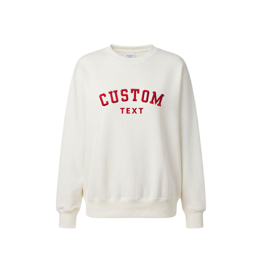 An off-white crewneck sweatshirt with 'CUSTOM TEXT' embroidered in red collegiate-style lettering on the chest, displayed against a solid white background.