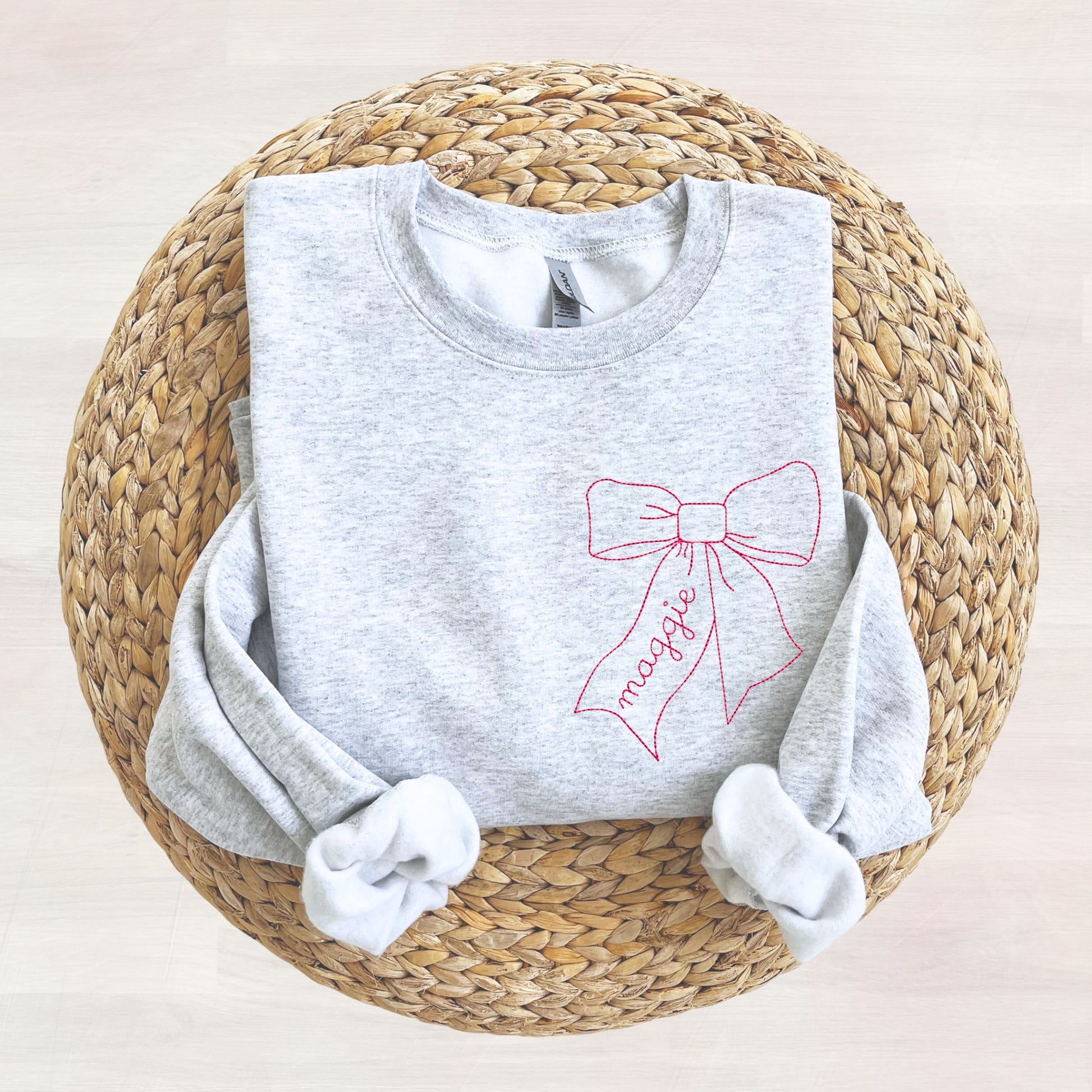 ash sweatshirt with a stitched raspberry pink bow name design on the left chest