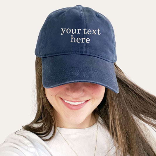 young woman wearing a navy hat with custom embroidered text in white thread 