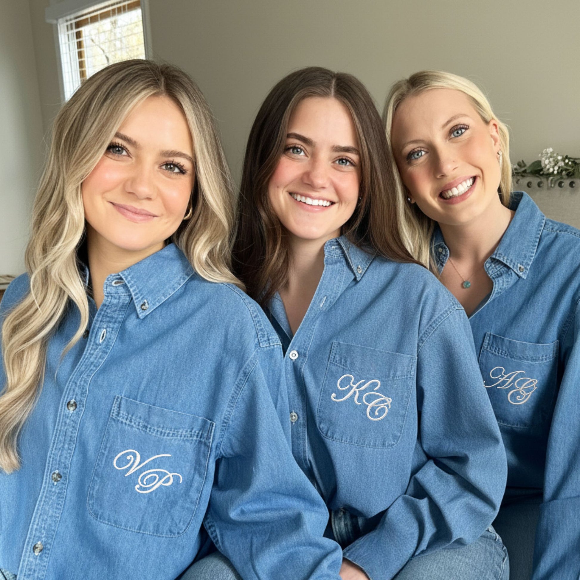 Three women wearing matching blue denim shirts with embroidered monograms in edwardian font