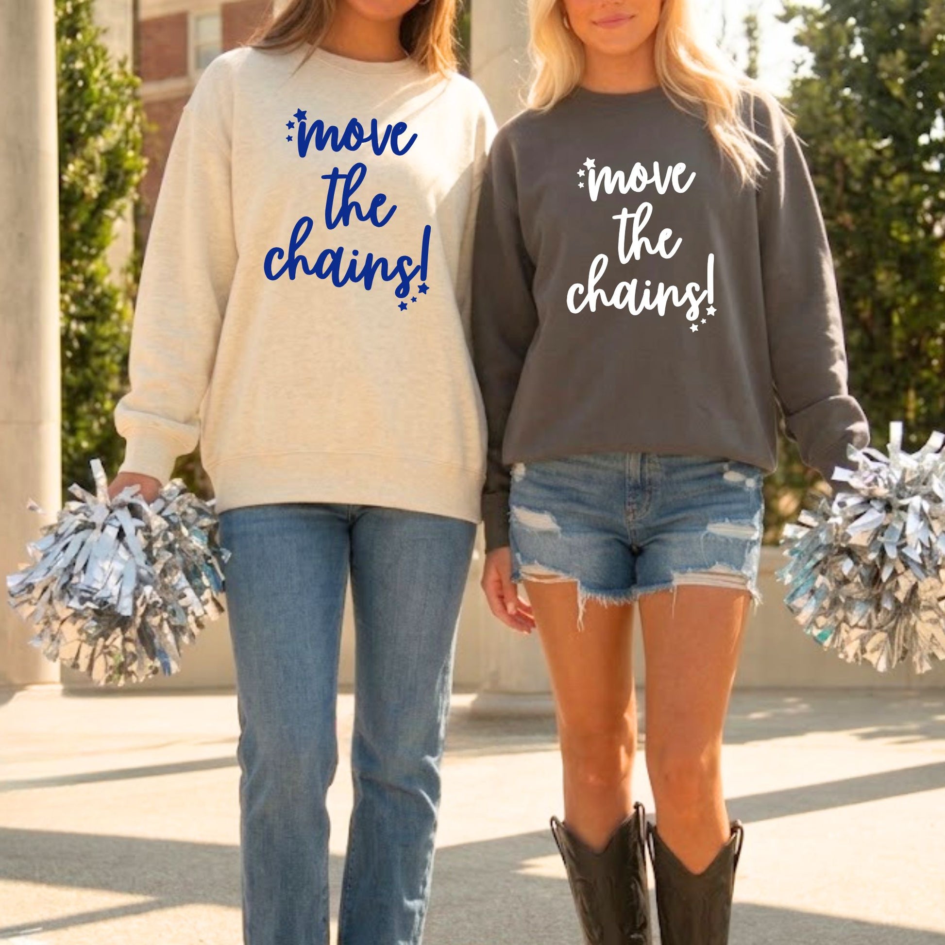 Two women standing outdoors wearing matching sweatshirts with the slogan 'move the chains!' in blue and white lettering. The woman on the left wears a cream sweatshirt with blue jeans, and the woman on the right wears a dark gray sweatshirt with denim shorts and boots.