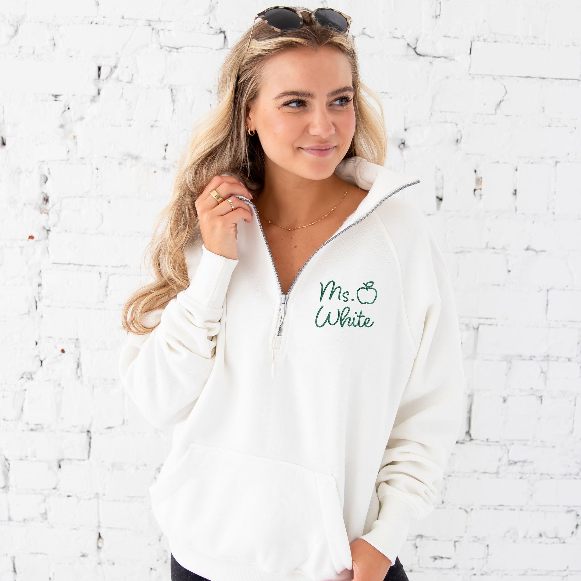 close up of woman wearing a white boxy ladies fit quarter zip pullover with a custom name and outlined apple embroidered in a hunter green thread.