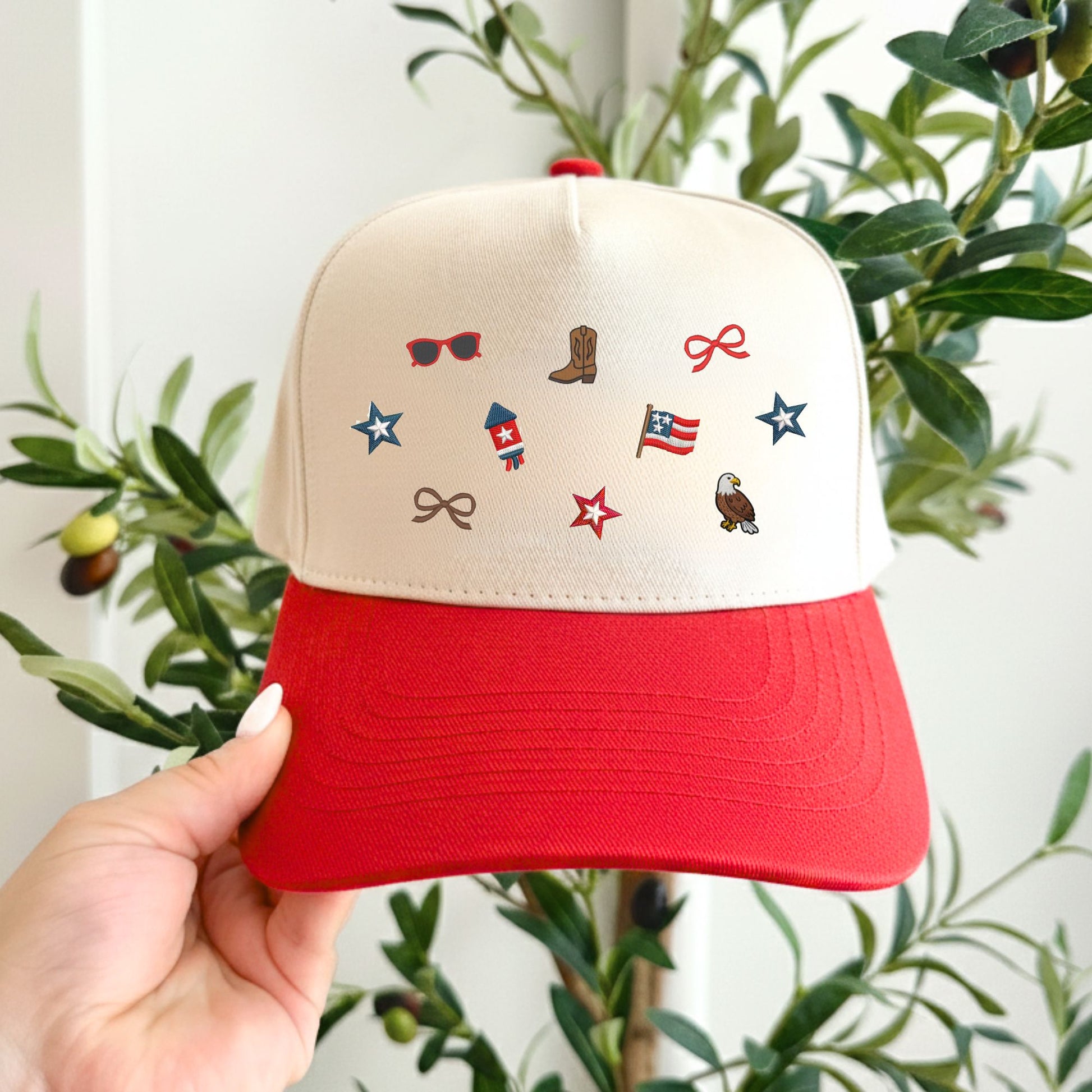 Beige and red cap with embroidered micro usa designs held in front of a plant