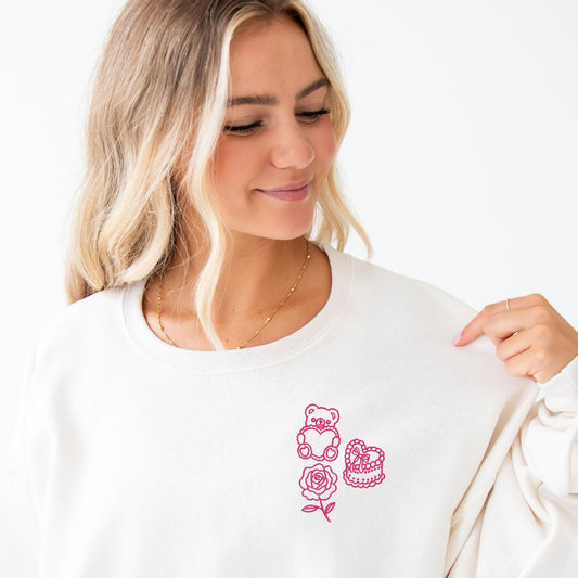 Woman wearing a sweet cream sweatshirt with pink coquette valentine's icons (teddy bear, cake, rose) on the left chest