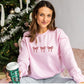 woman wearing a light pink crewneck sweatshirt with embroidered three bows cross the chest in red thread. 