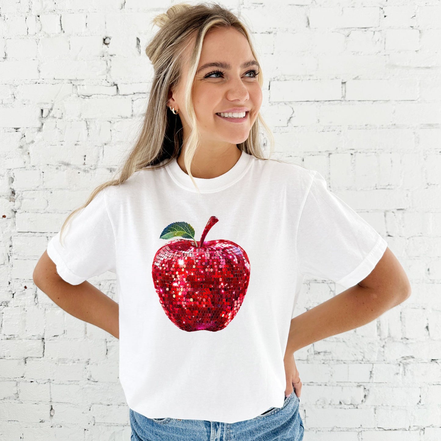 young woman wearing a white comfort colors t-shirt with large glitter apple print across the front of the chest