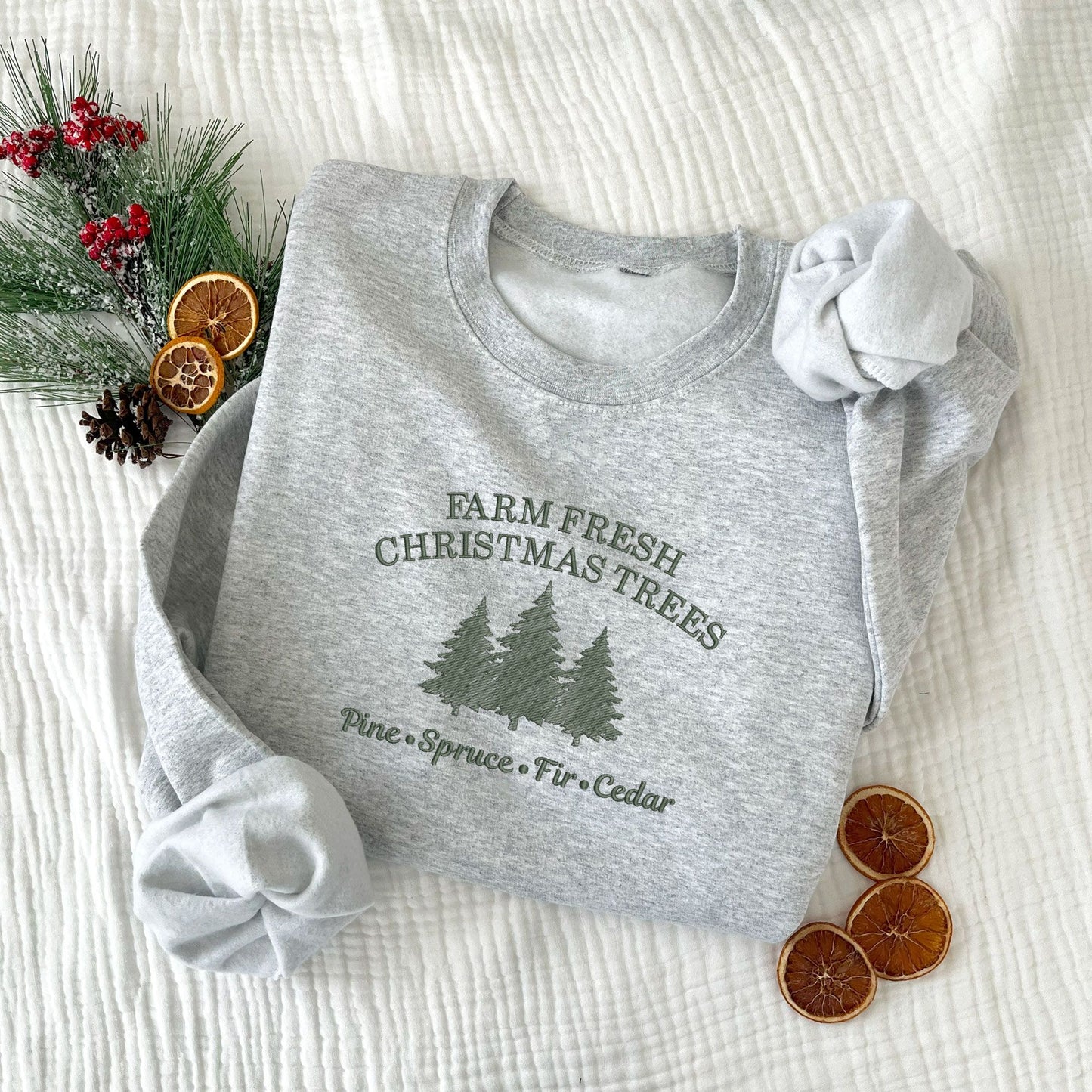 Christmas styled flat lay of an ash crewneck sweatshirt with embroidered farm fresh Christmas trees design with Christmas tree embroidery across the chest in ivy green thread