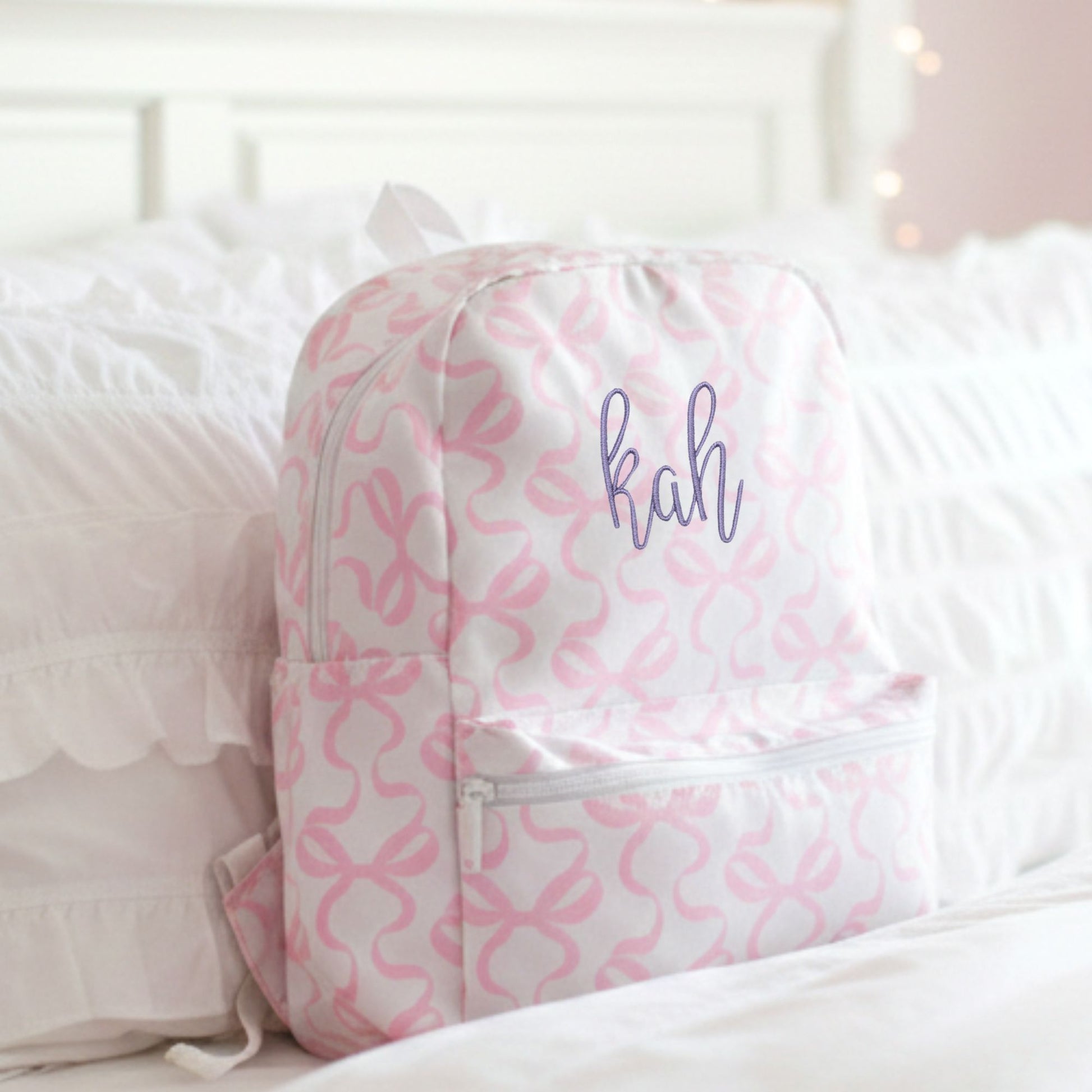 Pink and white bow patterned backpack with 'kah' text on a bed