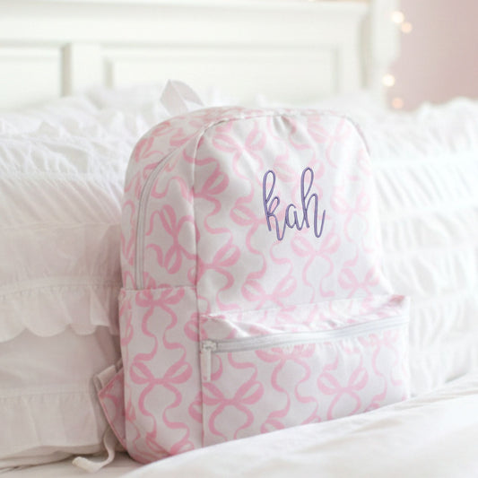 Pink and white bow patterned backpack with 'kah' text on a bed