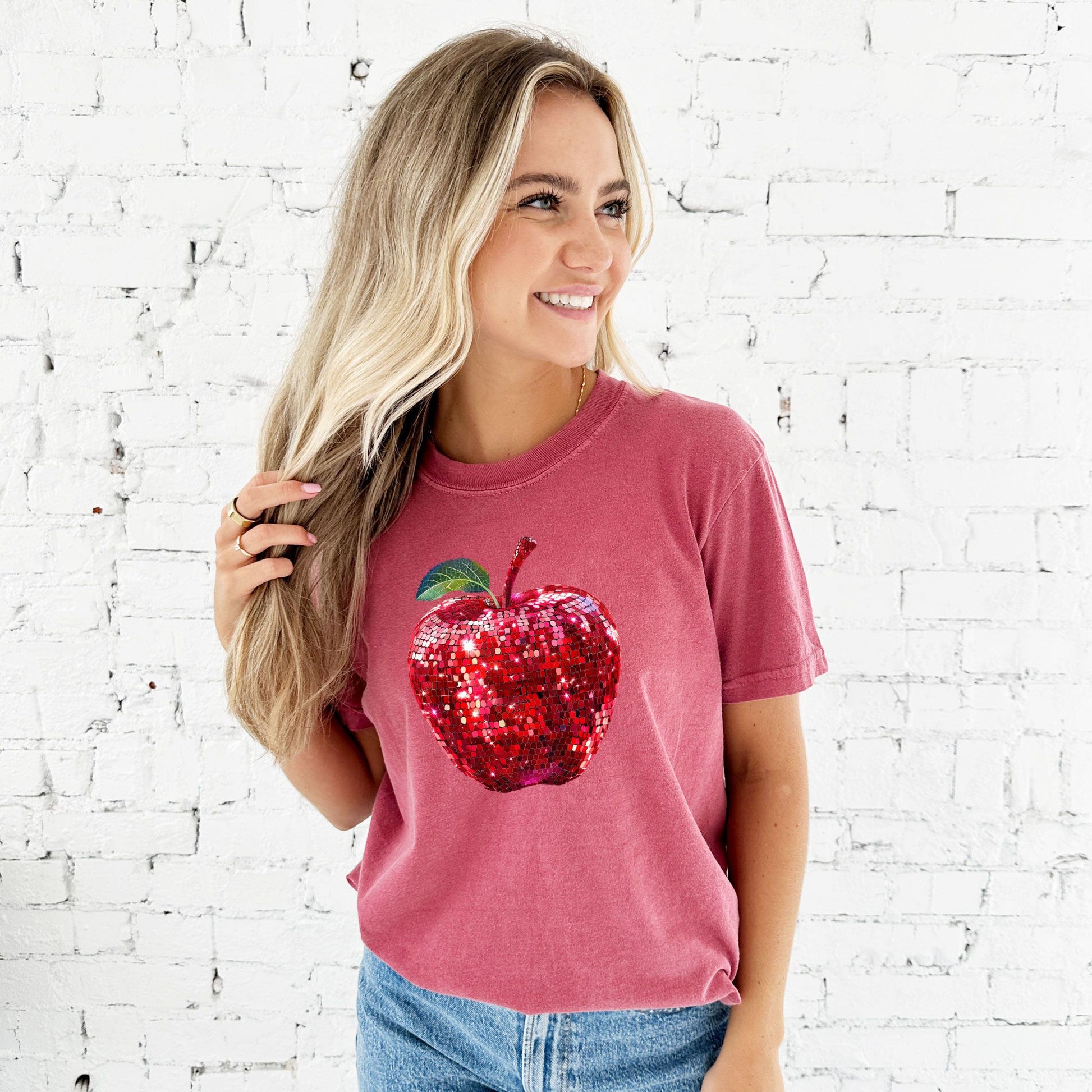 young woman wearing a crimson comfort colors t-shirt with large glitter apple print across the front of the chest