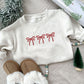 toddler natural heather crewneck sweatshirt with 3 embroidered bows across the chest in red thread.