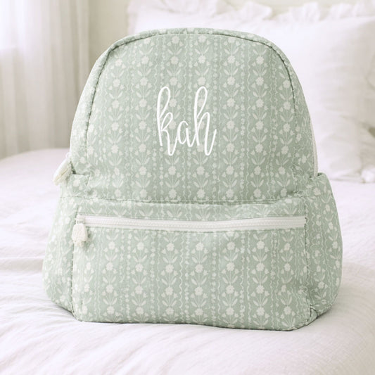 Sage green backpack with floral pattern and 'kah' monogram on a white surface
