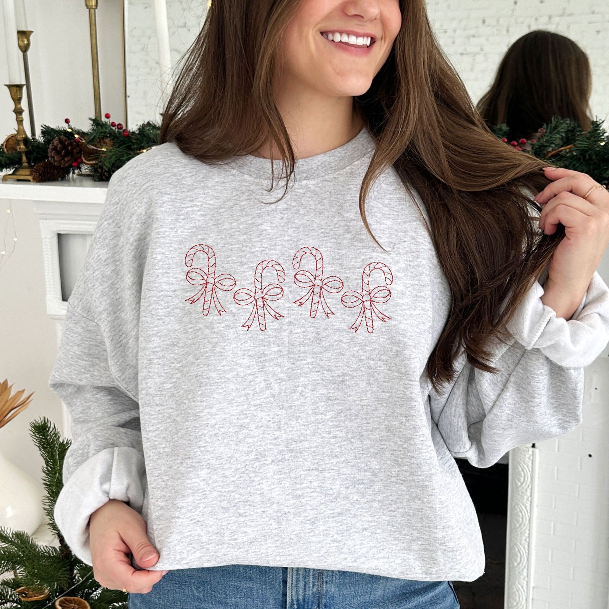 young woman wearing an ash crewneck sweatshirt with4 staggered outlined candy canes with bows across the chest in red thread.