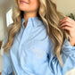 Woman wearing a blue button up shirt with monogrammed Edwardian script initials on the pocket  in a home setting