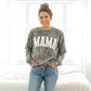 Woman wearing a camouflage sweatshirt with 'MAMA' printed on it, standing in a bedroom.