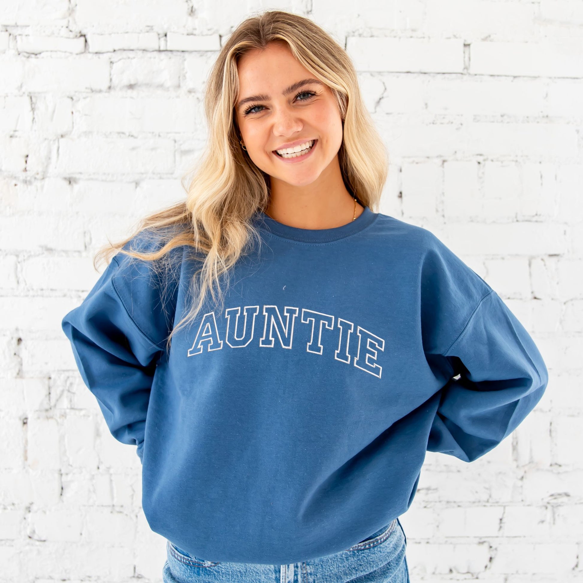 young woman wearing an indigo crewneck sweatshirt with embroidered AUNTIE in all caps athletic block font across the chest in white thread.