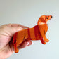 Hand holding a orange dachshund-shaped hair clip against a light background