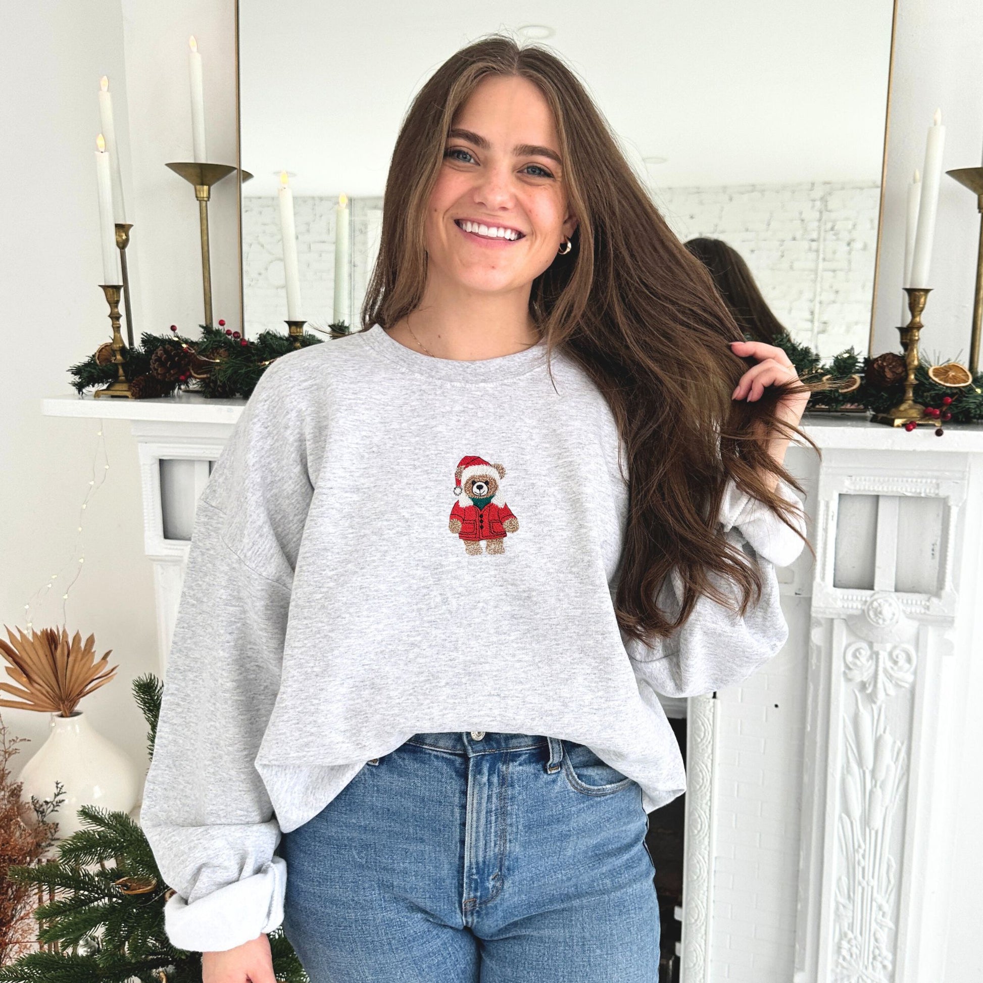 Woman wearing a gray sweatshirt with a teddy bear design in a festive indoor setting.