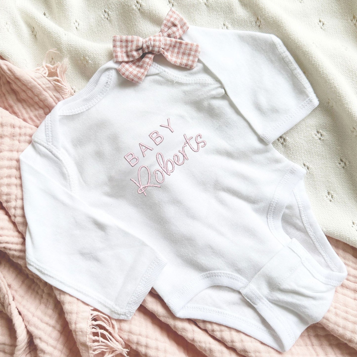 white infant bodysuit with custom baby Roberts embroidered on the center chest in powder pink thread