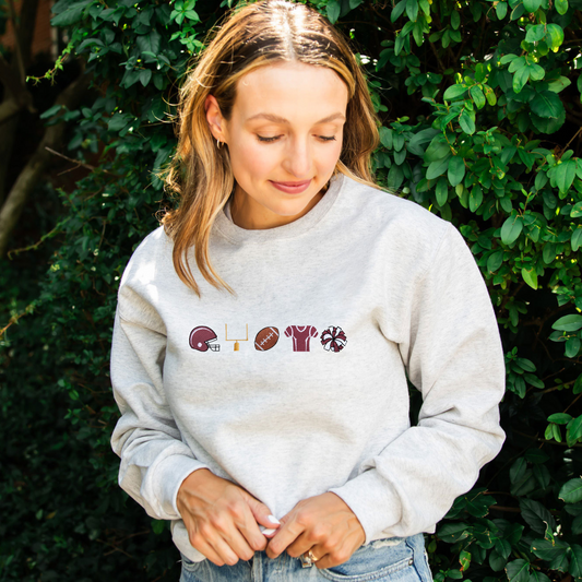 woman wearing a heather oatmeal crewneck sweatshirt with embroidered football icons across the chest with burgundy accent color