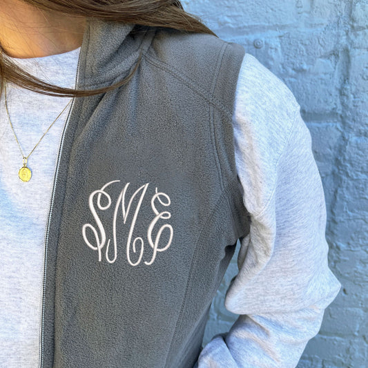 close up of young woman wearing a lightweight grey fleece vest with a white embroidered monogram on the left chest